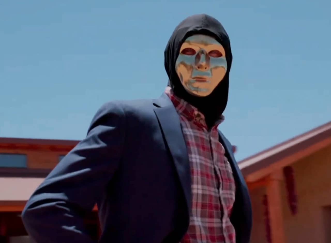 man in a flannel shirt and jacket with a gold face mask on