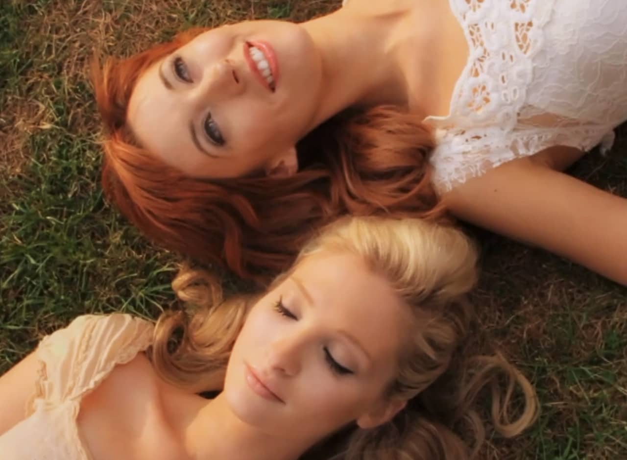 a blonde and a redhead woman lay in the grass