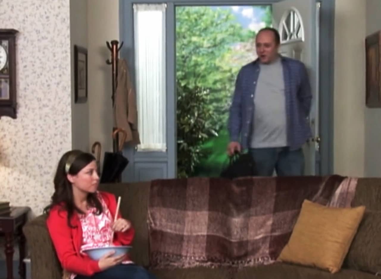 a man walks in the front door, his wife stirs a bowl on the couch