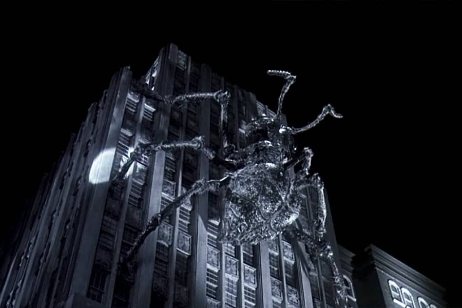 a giant ant scales a tall building with spotlights on it from below