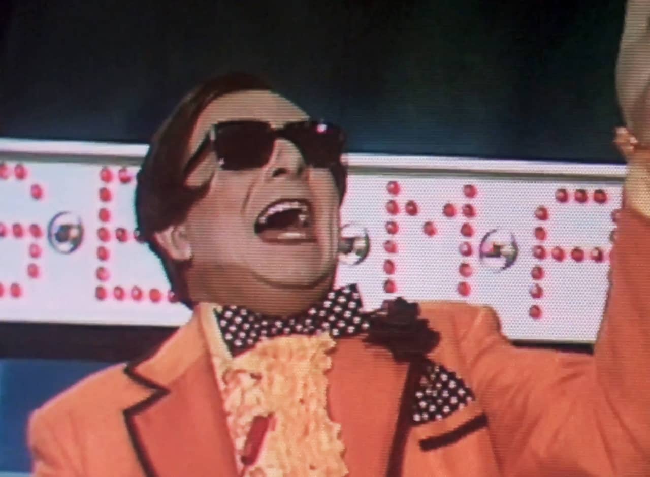 host Bert Schnick, in a bright orange suit with slick black hair and sunglasses