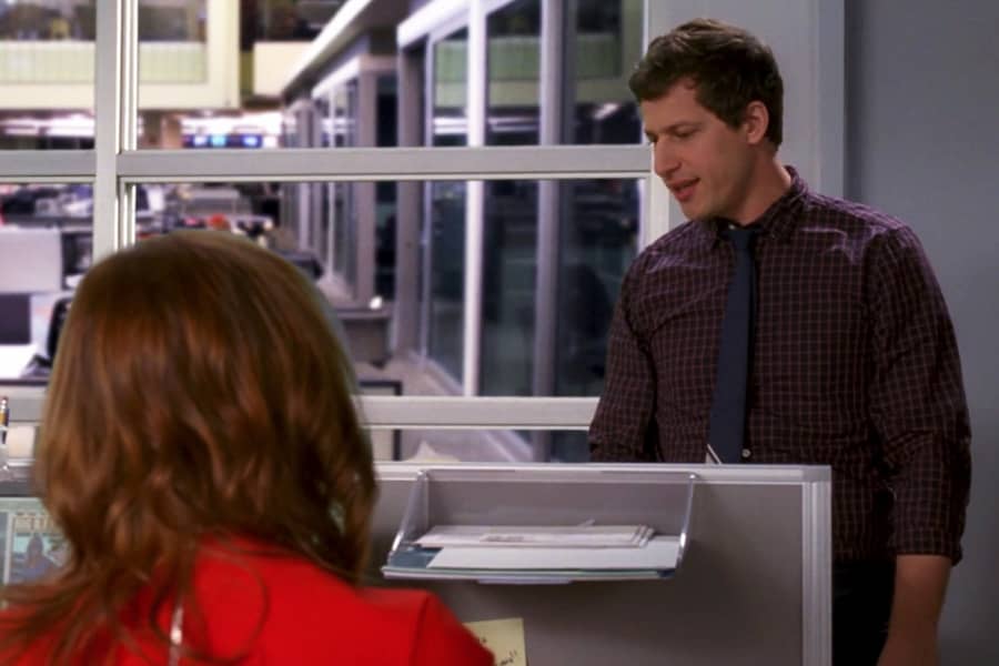 Andy Samberg talks with Emma Stone in an office