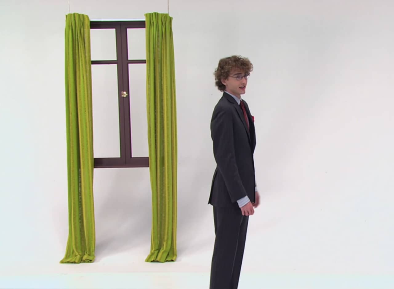 Sinjin, a teen boy, standing in a white room with a window with green curtains