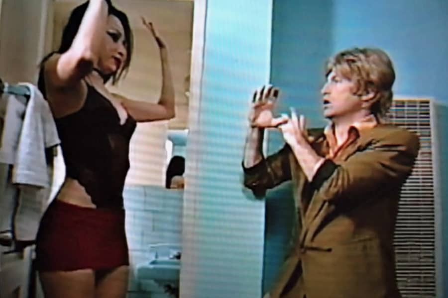 Gil gets into a fighting stance as another woman walks out of the bathroom with her hands up
