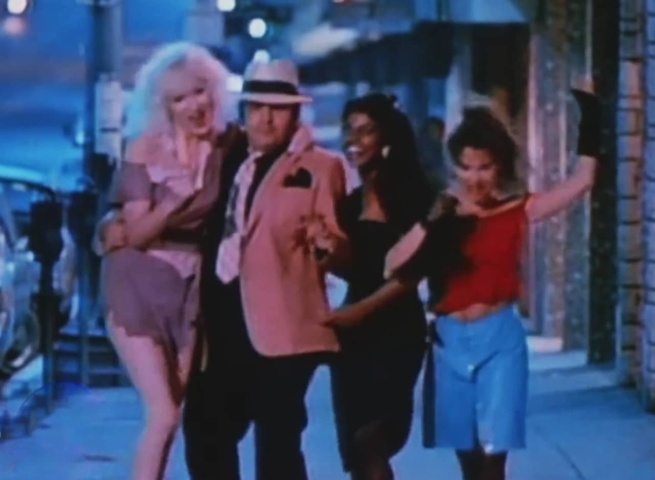 Nunzio, a gangster, walking down the street surrounded by three women