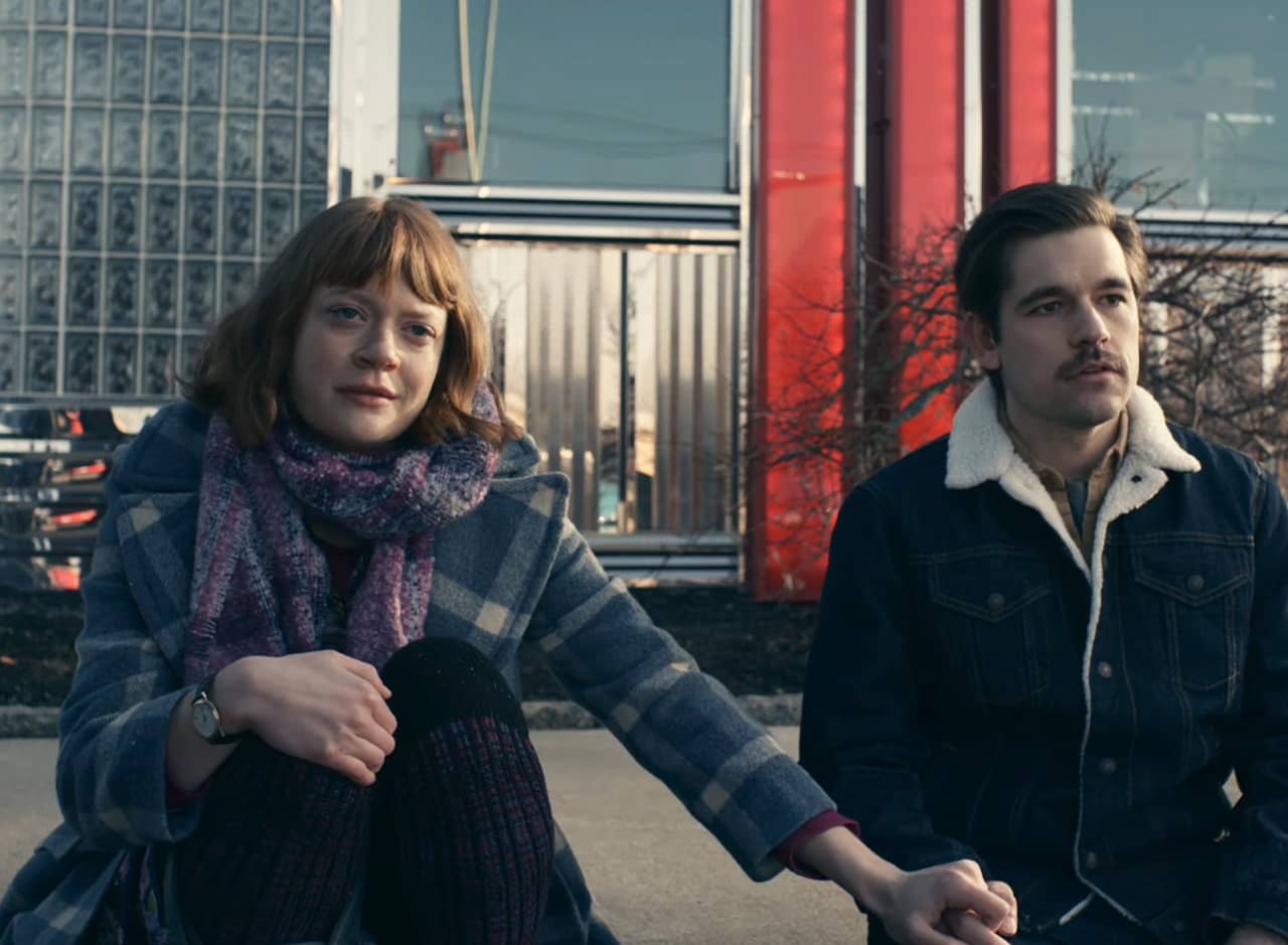 a young man and woman sit solemnly on the curb outside a diner
