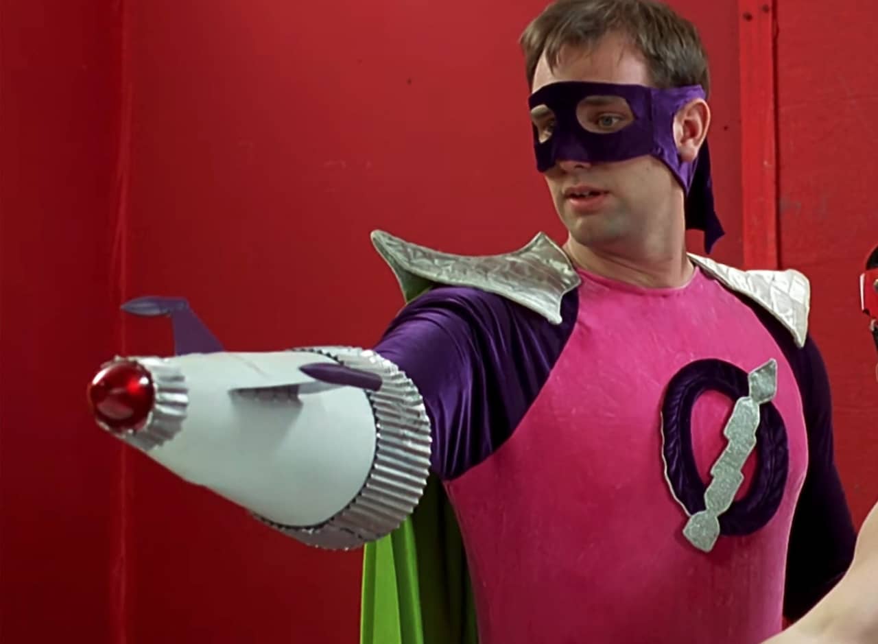Orgazmo in low-budget superhero costume holding up a futuristic weapon