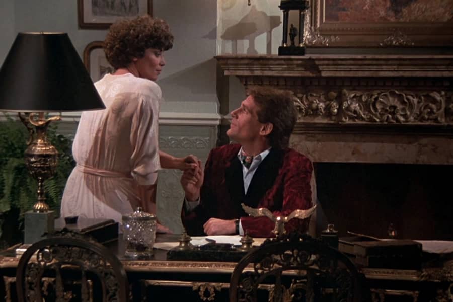 woman sits on a desk where a man grabs her hand