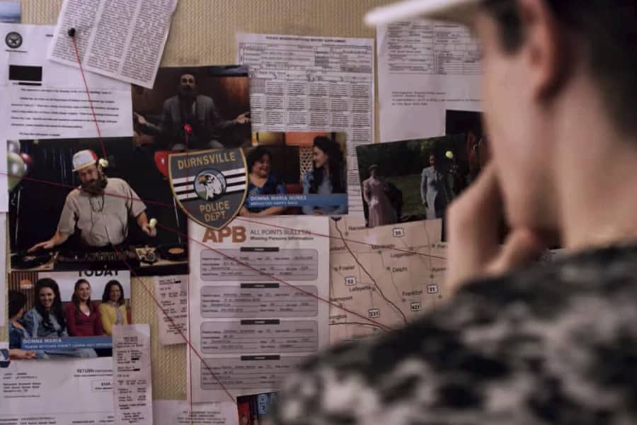 DJ Fingablast looks at a bulletin board covered in newspaper clippings, photos, and connecting strings