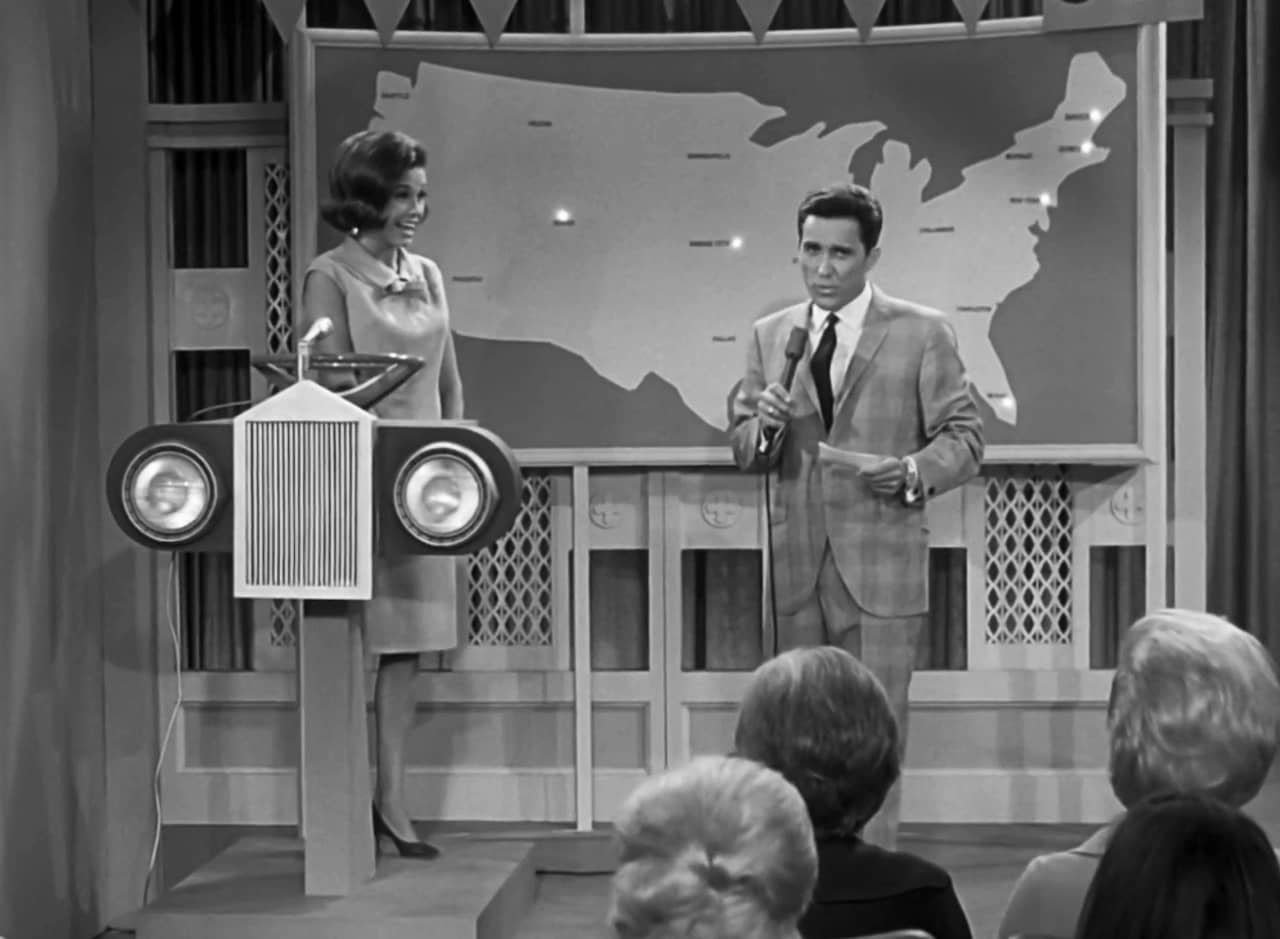 Johnny Patrick on a game show set with a giant map of the U.S. and Laura Petrie is the current contestant