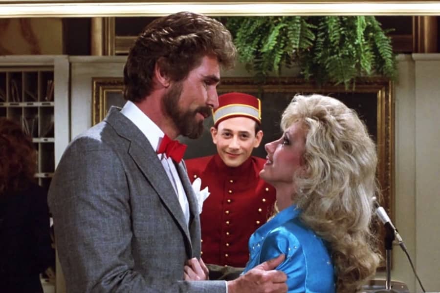 Pee Wee and Dottie look at each other and between them the real Pee Wee Herman cameos as a bellhop