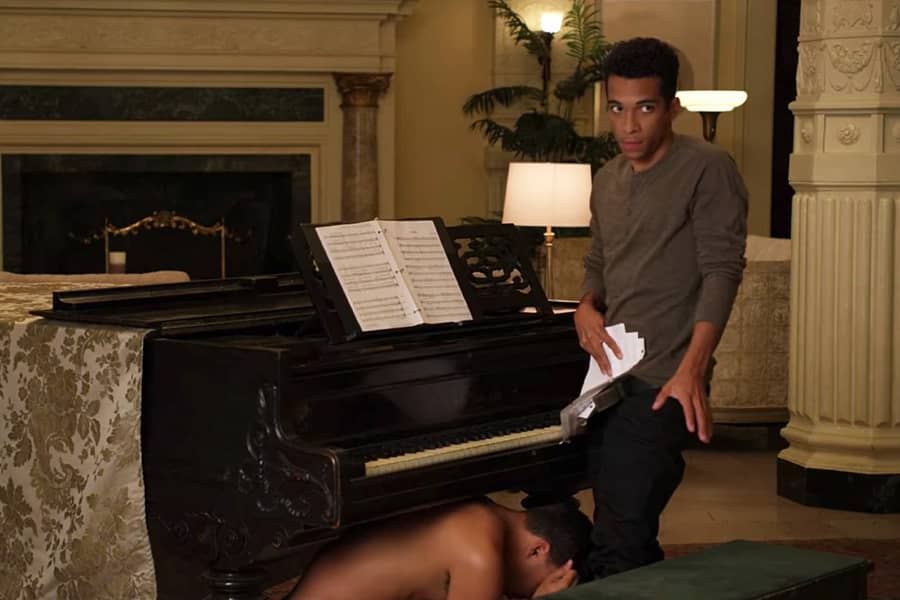 Cupcake’s son covers his crotch with papers while another shirtless boy crouches underneath the grand piano