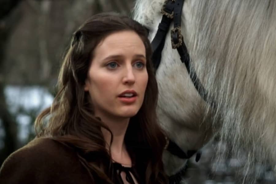 a brunette woman stands next to a white horse