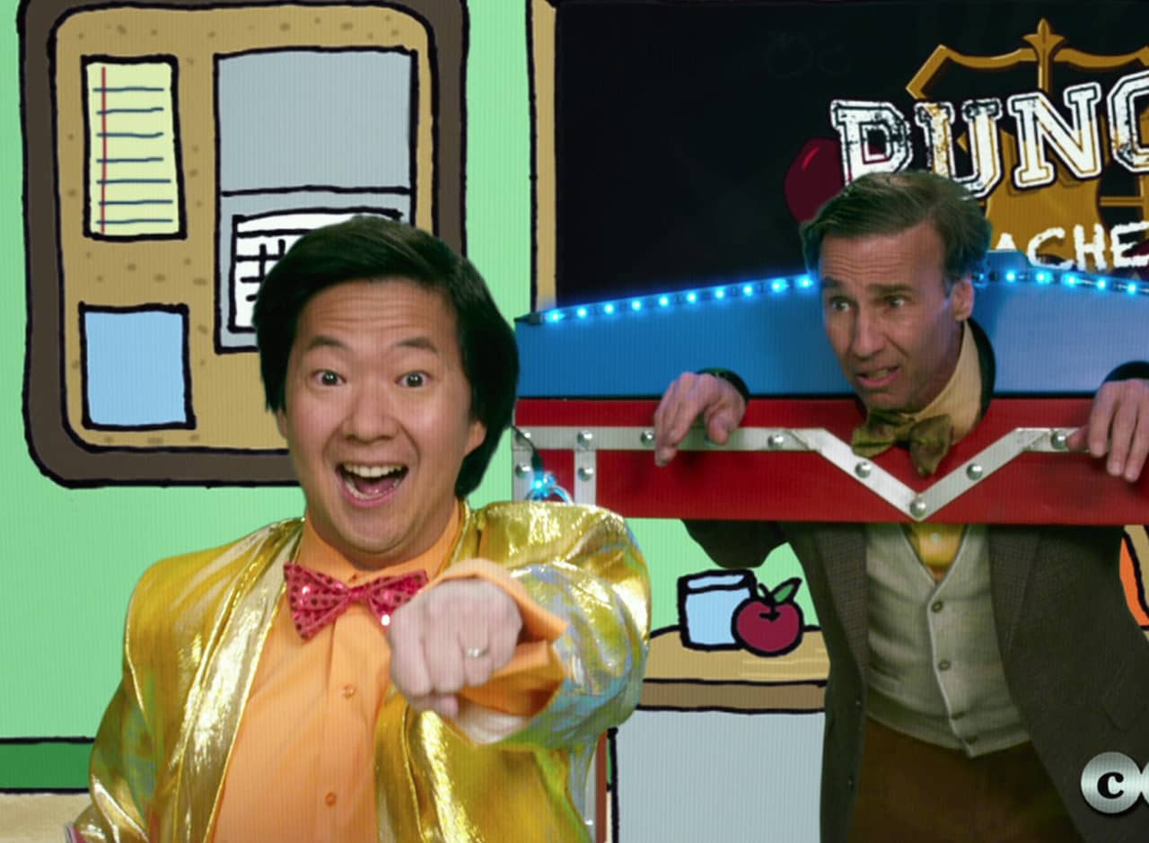 excited game show host in a bright bow tie stands in front of a distraught teacher with his hands and head in stocks