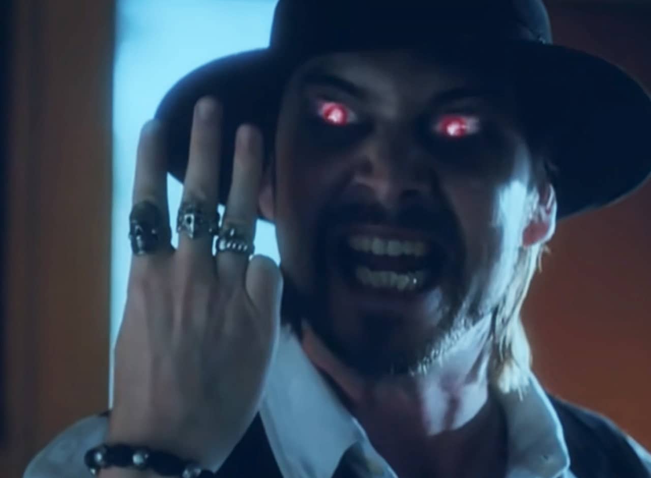 Hades, a fedora-wearing bro with glowing red eyes, holds up three fingers 