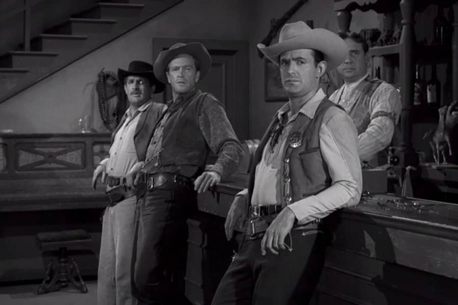 McGrew leaning against the bar with two other men