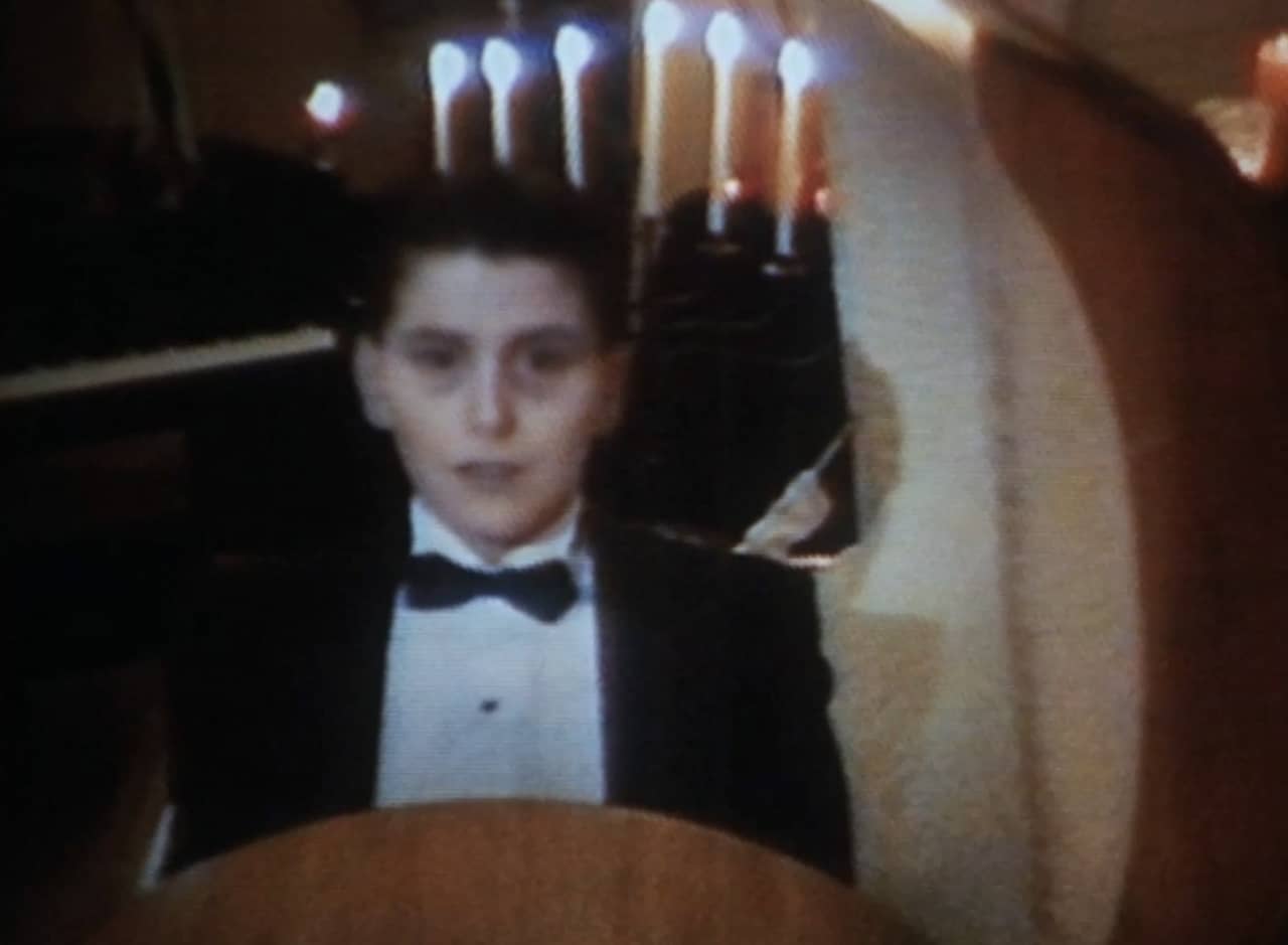 dead teen boy in a tux sitting up inside a coffin in a dark, candle-lit room
