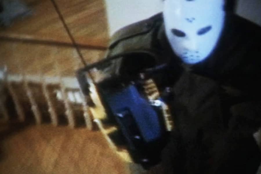 man wearing a hockey mask and holding a chainsaw climbs up the stairs