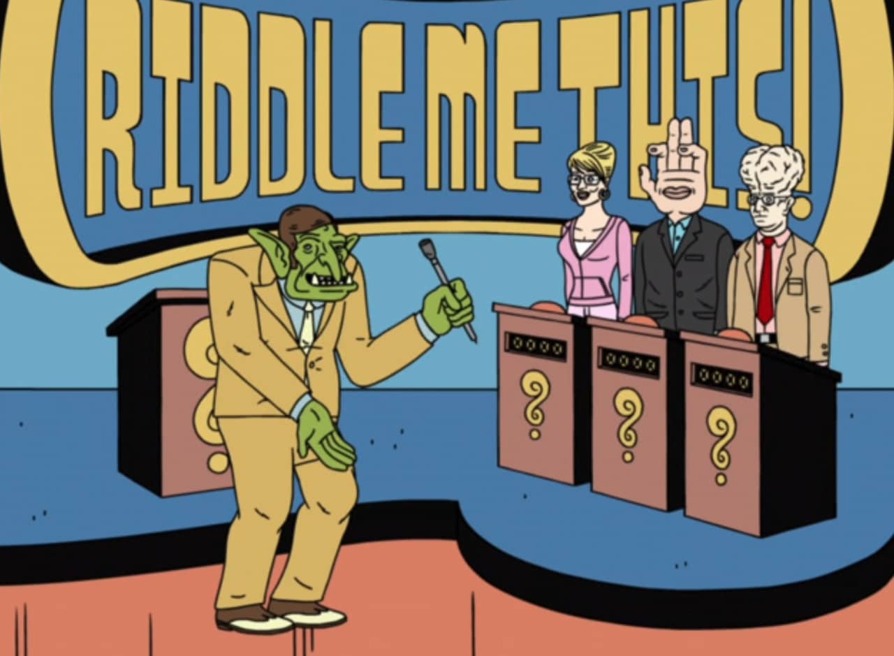 Quaggle on set with three contestants: a woman with glasses, a man with a giant hand for a head, and a man with a giant brain bulging in his skull