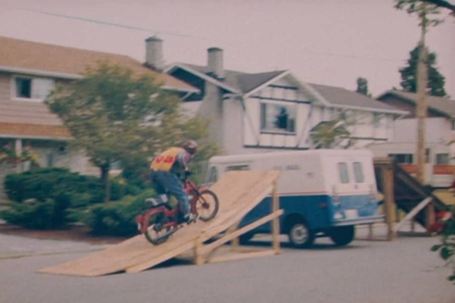 Rod riding a motorbike up a plywood ramp to try and jump over a van