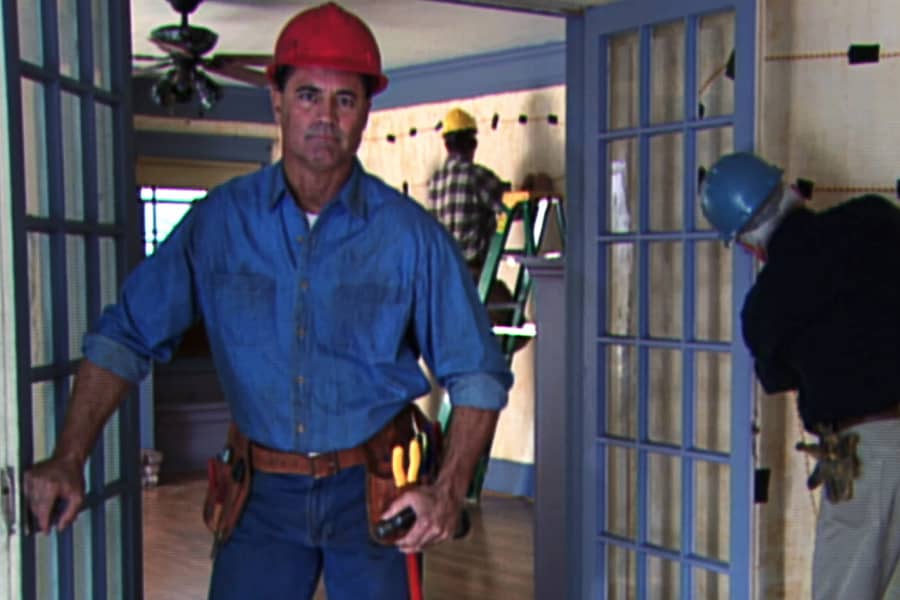 Rusty in a house while men set up explosives on the wall