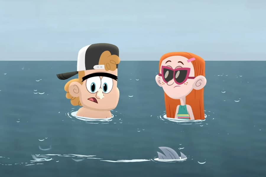 boy and girl chest-deep in the ocean as a small fish fin swims by