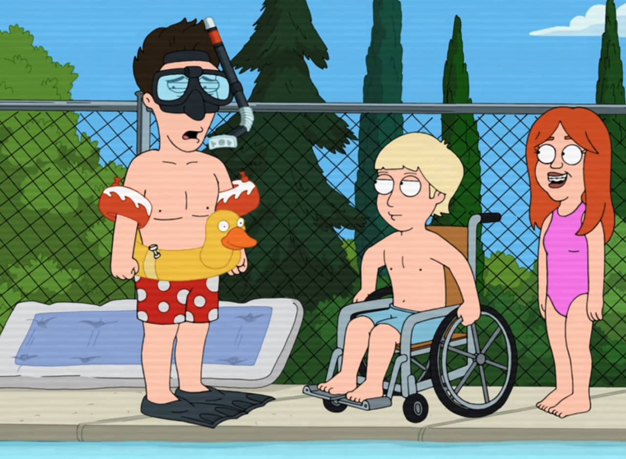 David Schwimmer at a pool wearing fins, inflatable tube, arm floaties, and a snorkel mask; he’s standing by a boy in a wheelchair and a girl with braces