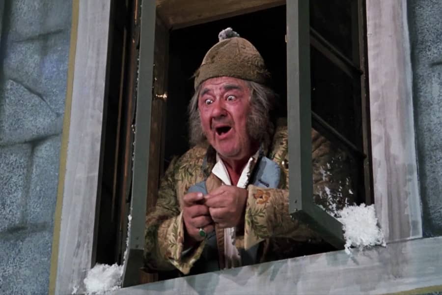 Scrooge excitedly looks out his bedroom window