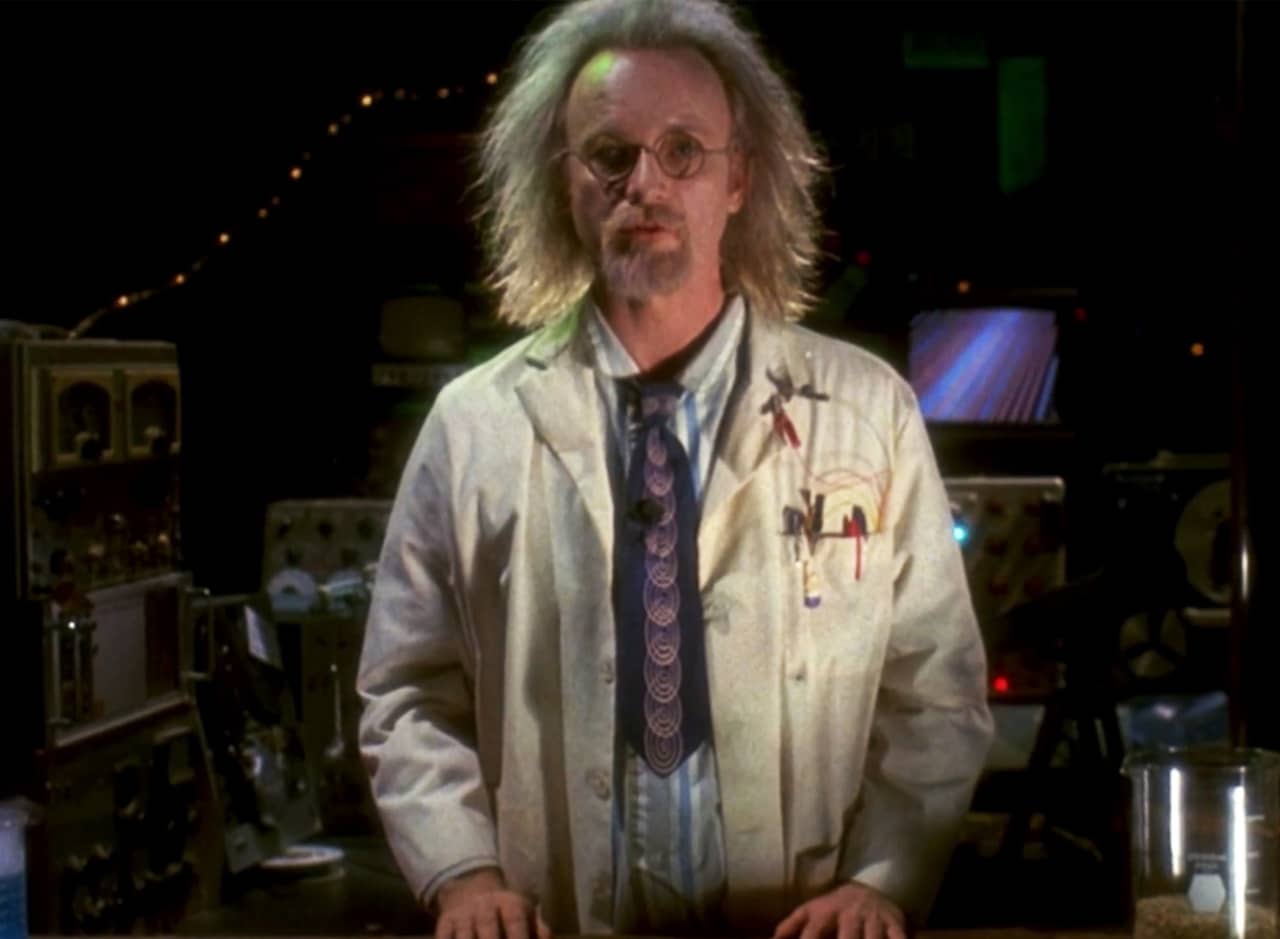 Philo, a man with wild white hair, in a lab coat in a dark lab