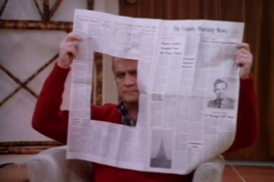 Dick Loudon as Henry Bumpter, looking through a hole cut out of his newspaper
