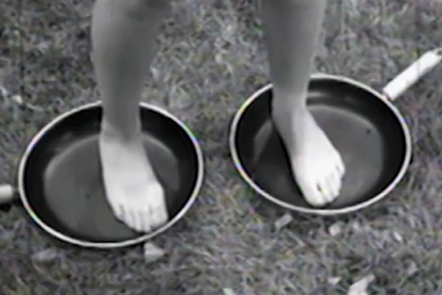 two bare feet standing on frying pans on the grass