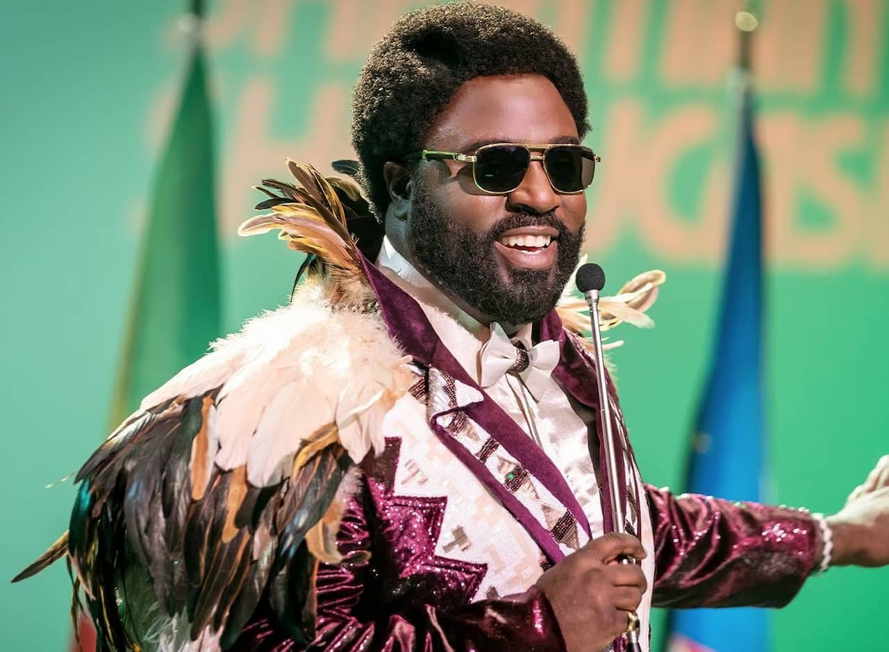 Sherman McDaniel wearing a purple sequin suit and holding a microphone