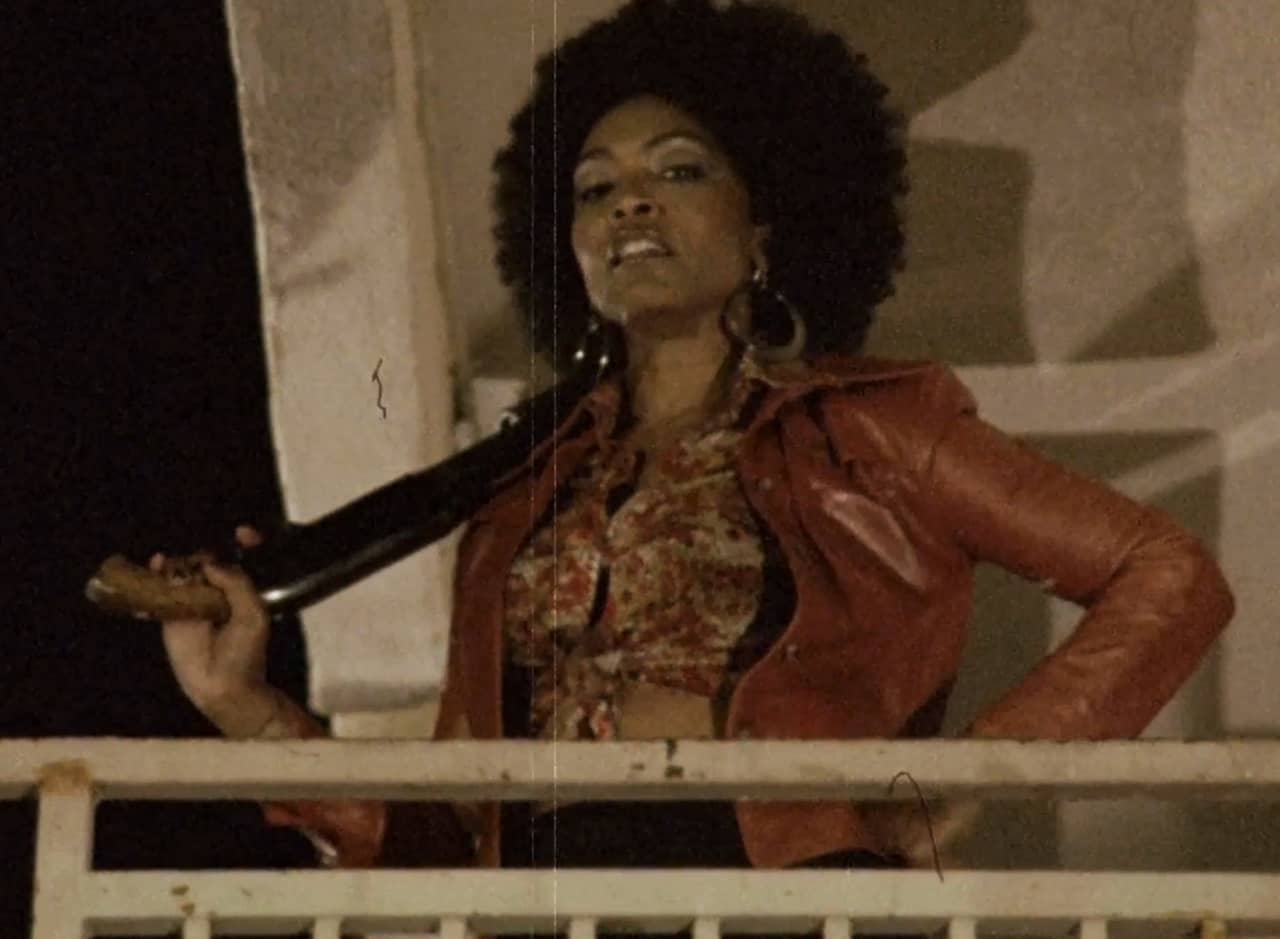 Ramona Royale with afro and big earrings holds a shotgun over her shoulder