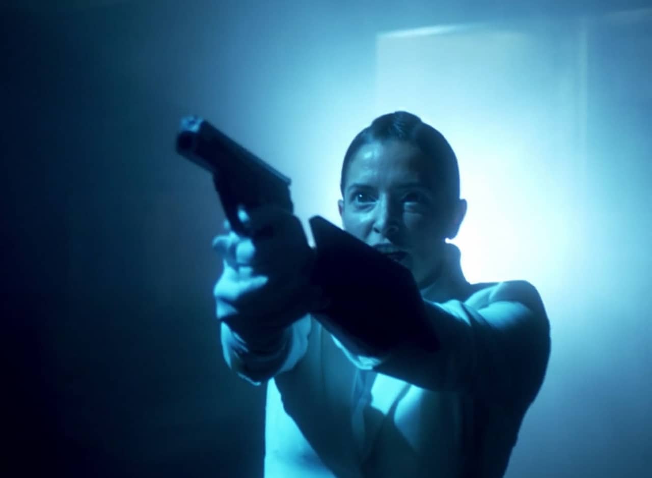 a woman in uniform and bathed in blue light points a gun offscreen