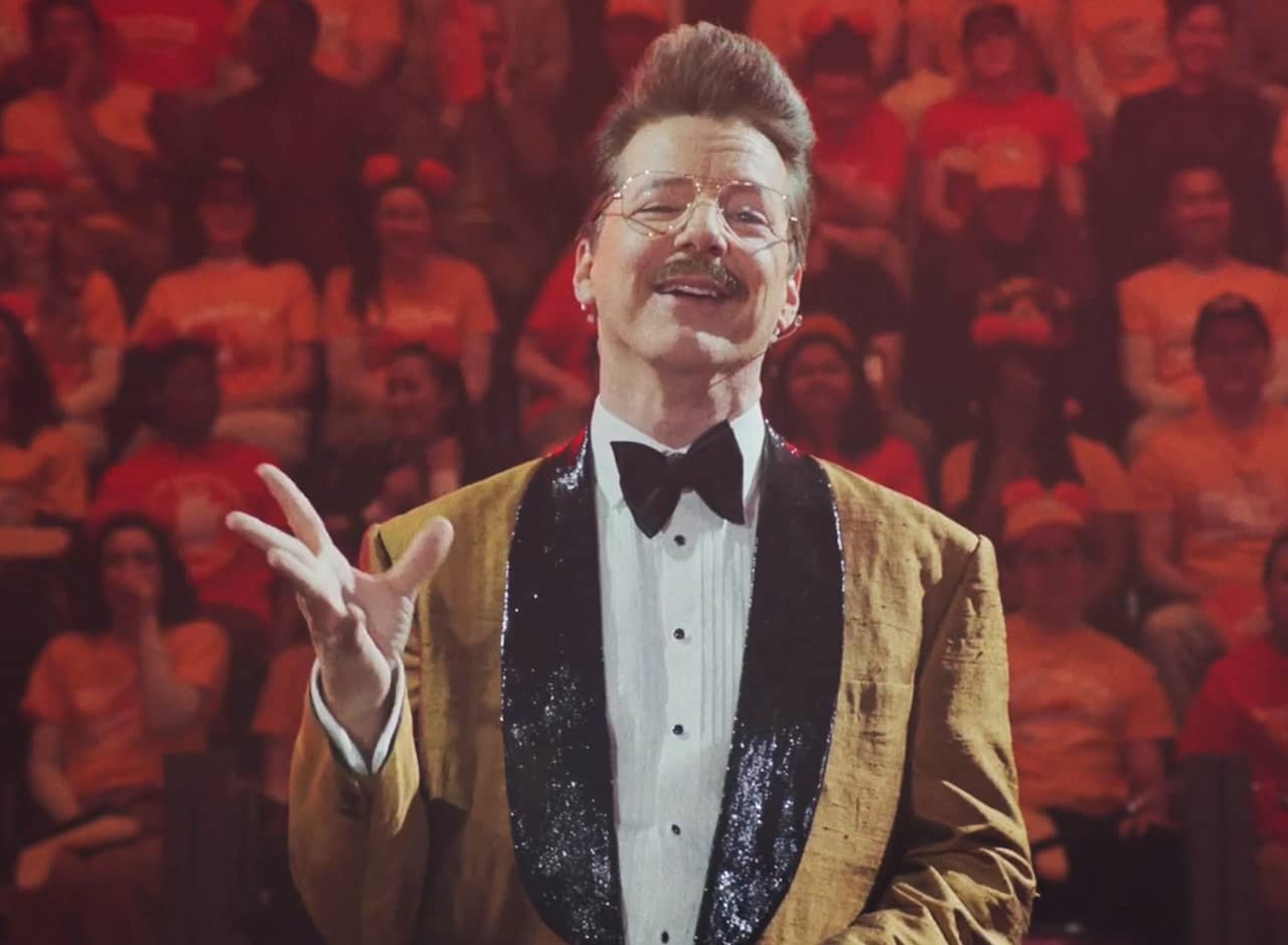 mustached host Gary Greenbacks wearing a mustard jacket with black sparkly lapels