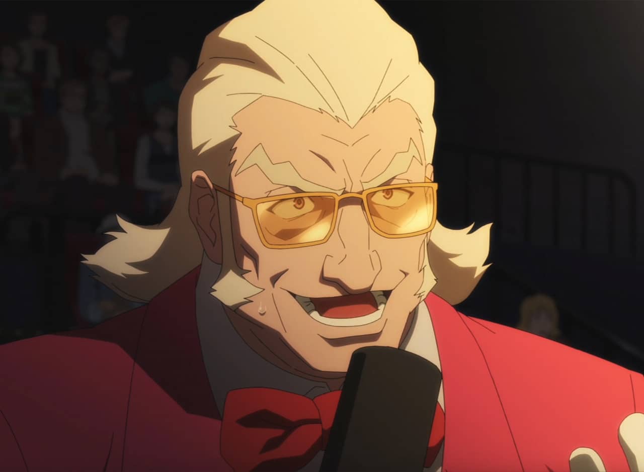 Stan Sullivan, a man with white slicked back hair and long sideburns, wearing tinted glasses and speaking into a microphone