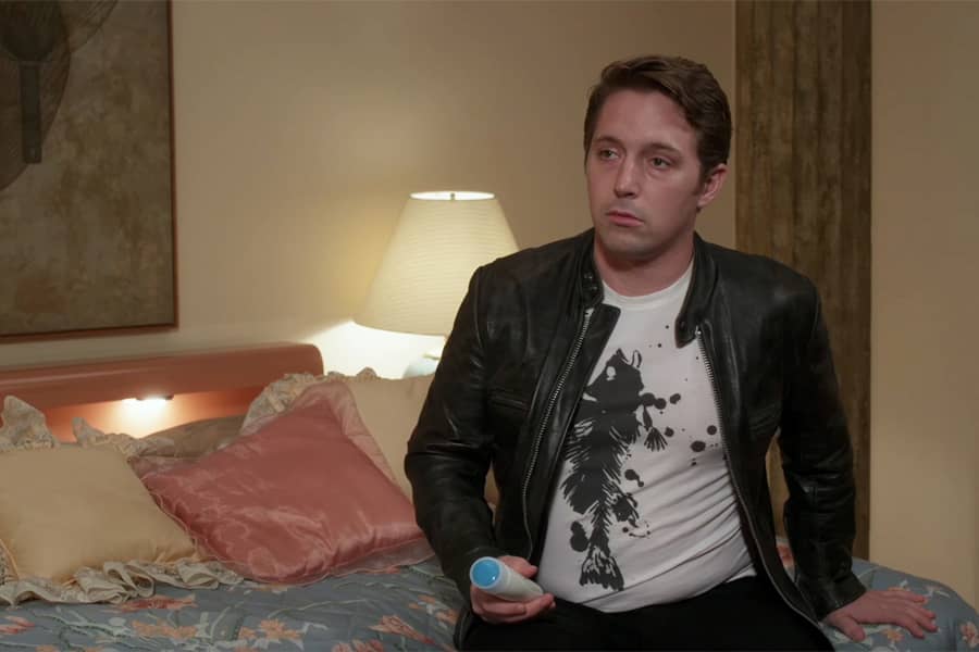 man in leather jacket sitting on a bed