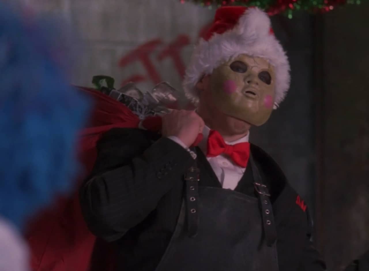 a man in a creepy baby mask and apron wearing a santa hat