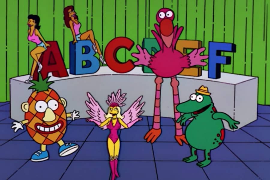 a stage with giant alphabet letters, Xoxchitla in feathered dress, a pineapple character, alligator charator, and giant flamingo character