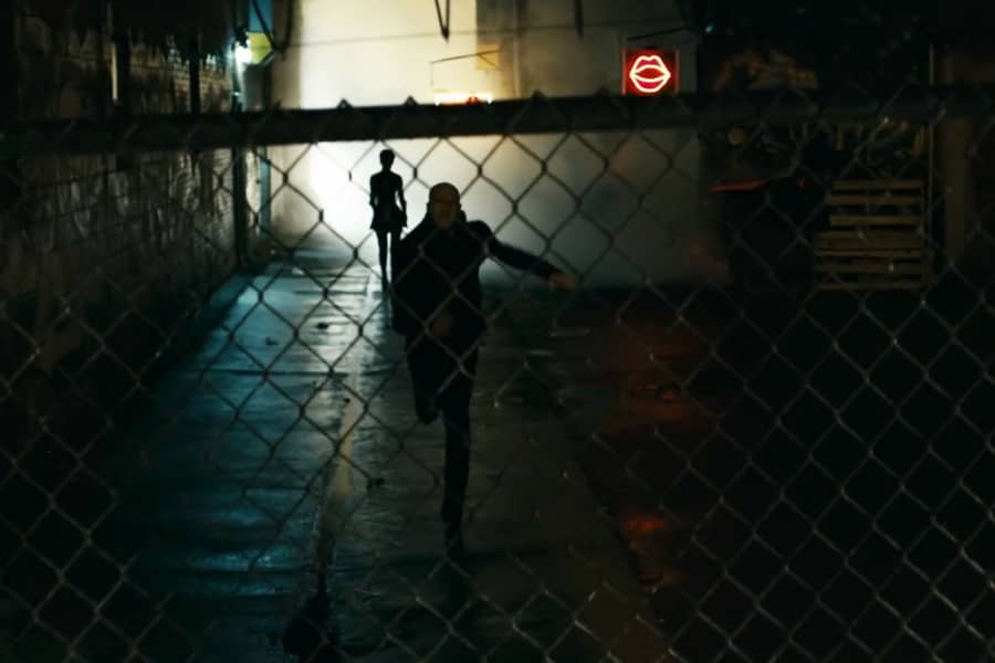 a man runs down a dark alley with a woman following behind