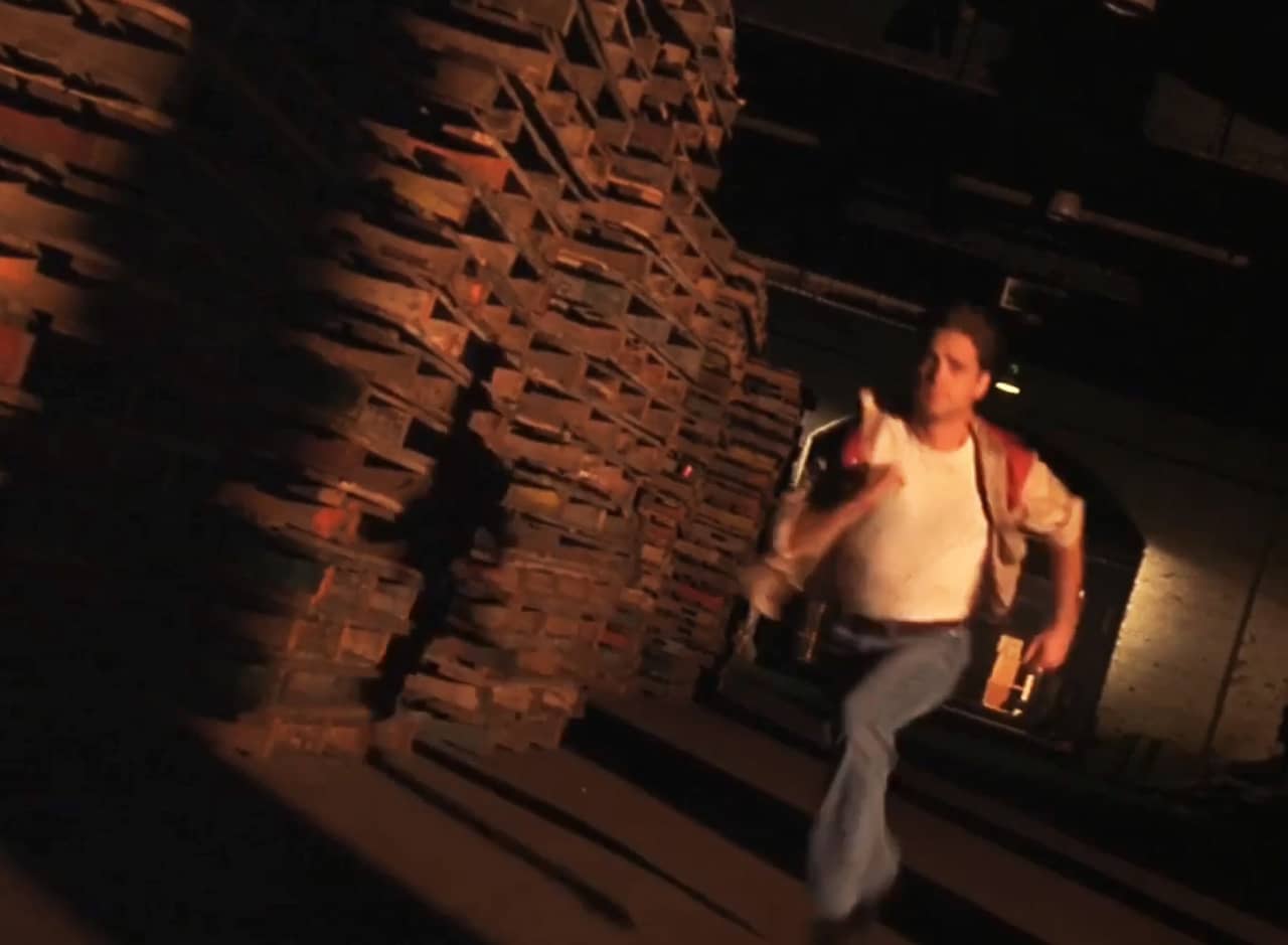 Ronnie Bostock as Johnny running through a dark warehouse next to a pile of shipping pallets
