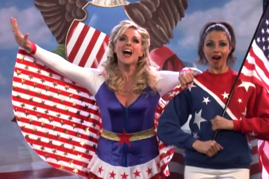 Maroney in a patriotic outfit singing next to a woman holding an American flag