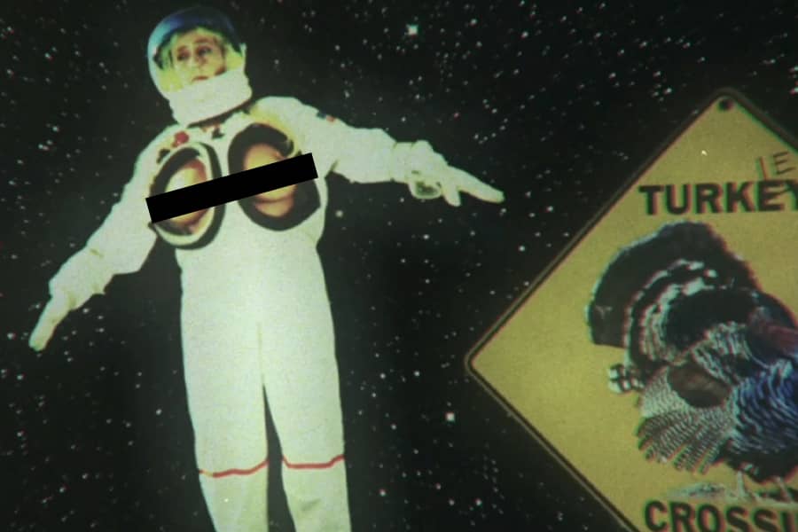 woman in astronaut suit floating in space, but her breasts are exposed; floating nearby is a Turkey Crossing road sign