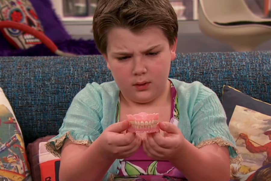 young son holding up a pair of dentures