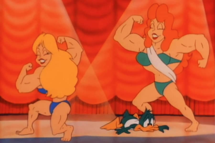 contestant, Plucky Duck, laying on the floor next to two super buff wrestler women