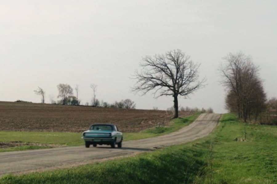 a vintage blue car drives down a rural road