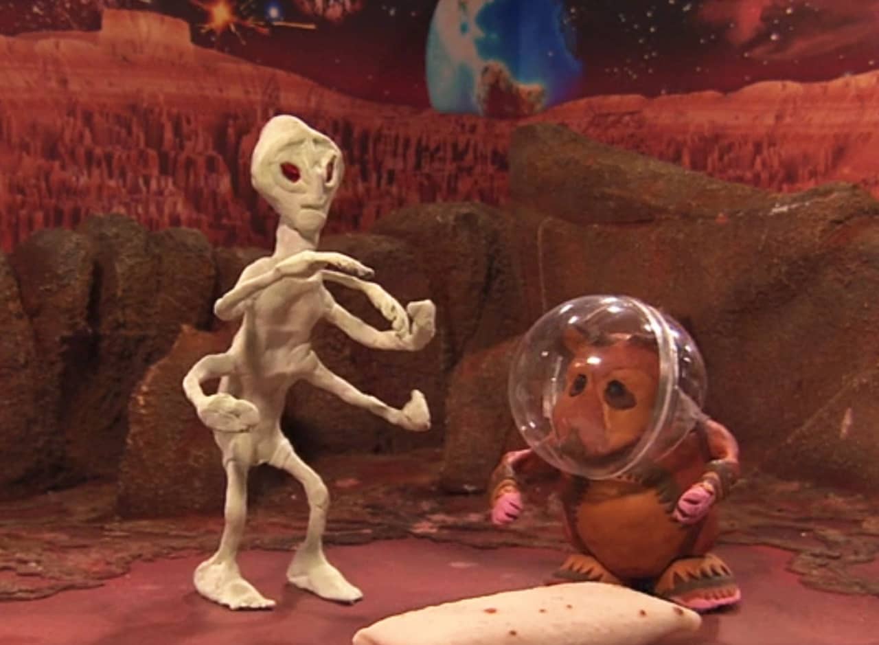 model of a five-armed space alien next to a hamster figure with a space helmet on standing next to a burrito