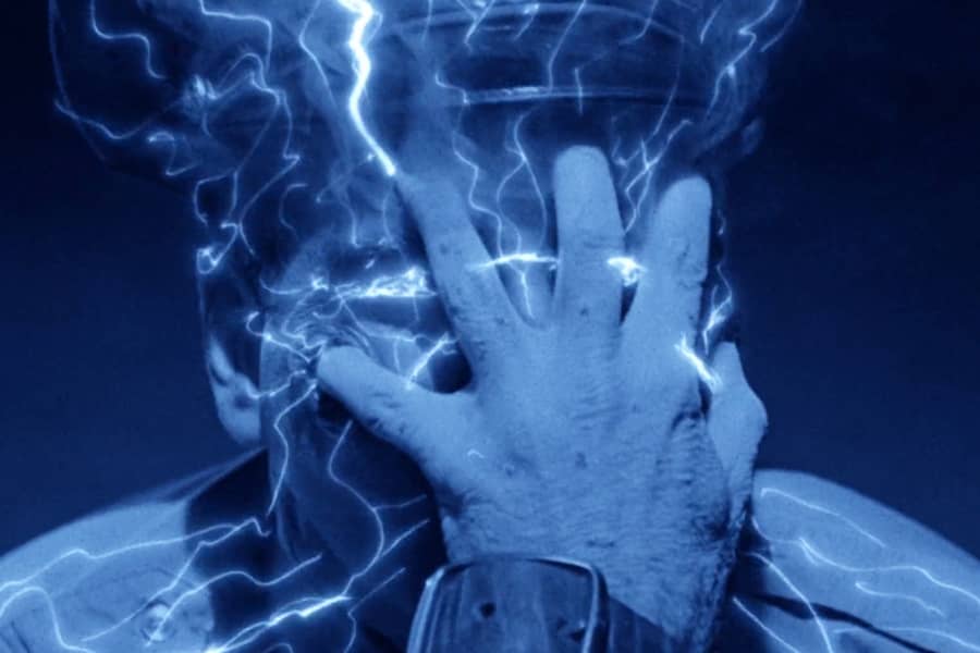 a man’s hand grips another man’s face, sending electricity throughout his head