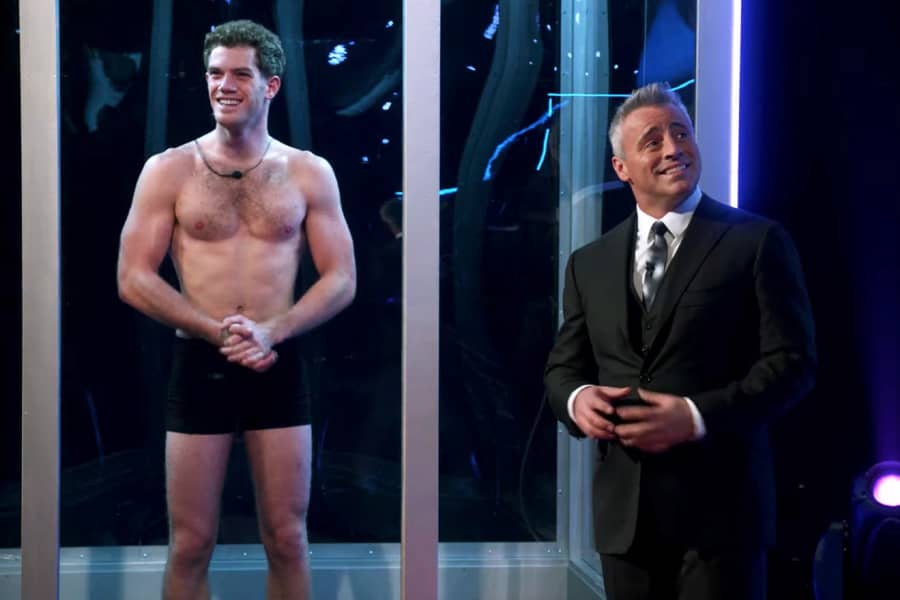 Matt LeBlanc smiles outside one of the boxes, a half-naked man stands inside