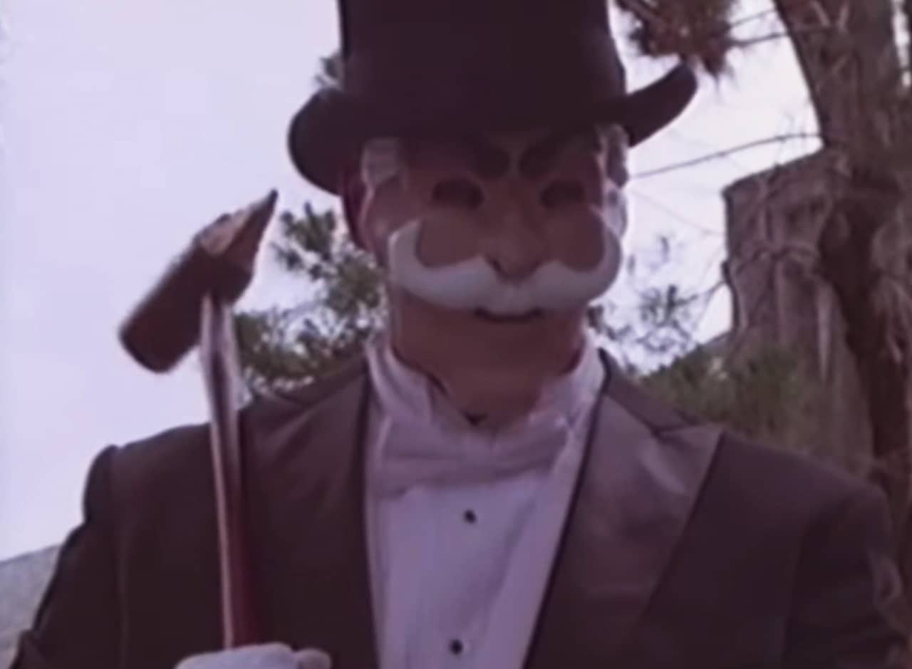 the killer dressed in a tuxedo, wearing a mustached mask, and holding a sharp spike